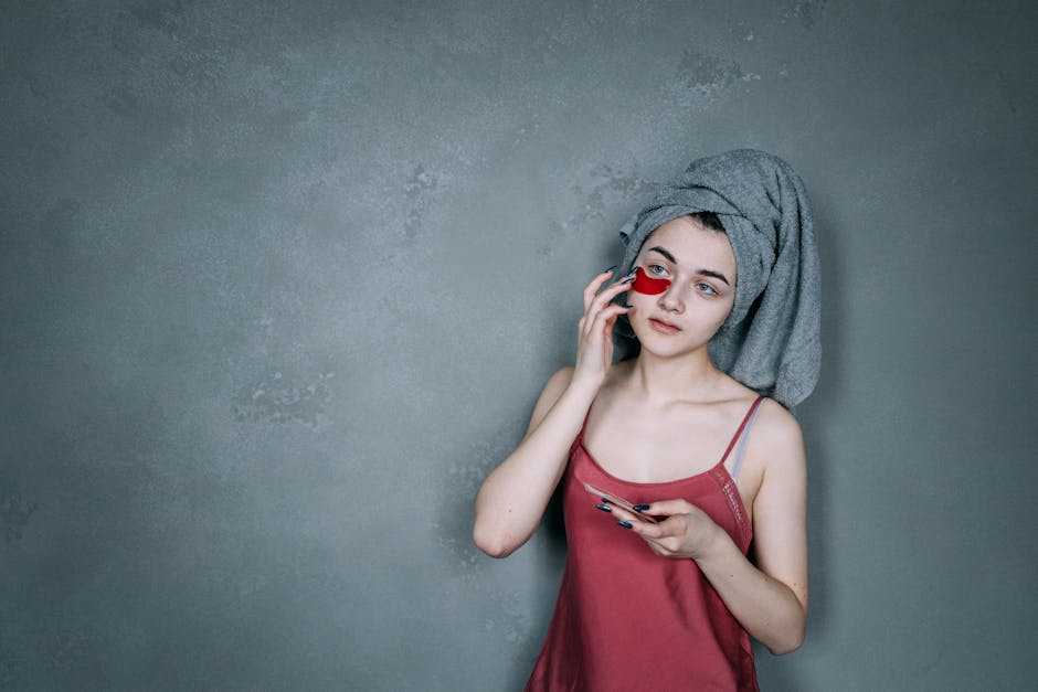 A young woman in a towel applies a rejuvenating under eye patch indoors.