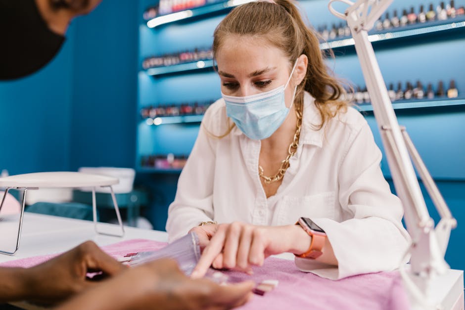 A young woman wearing a mask provides a manicure service in a modern salon setting.