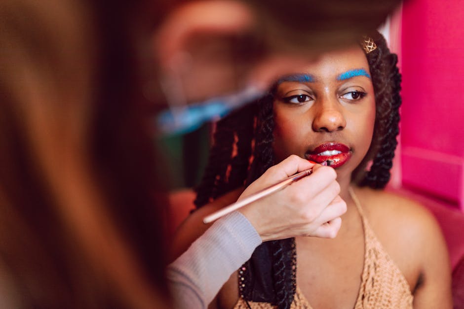Close-up of makeup artist applying bold lip color to a model with blue eyebrows.