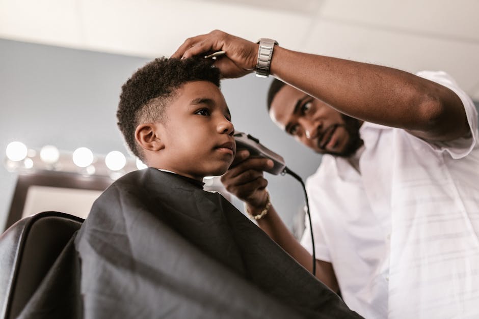 A barber skillfully trims a young boy's hair using clippers. Indoor barbershop setting with focus on grooming.