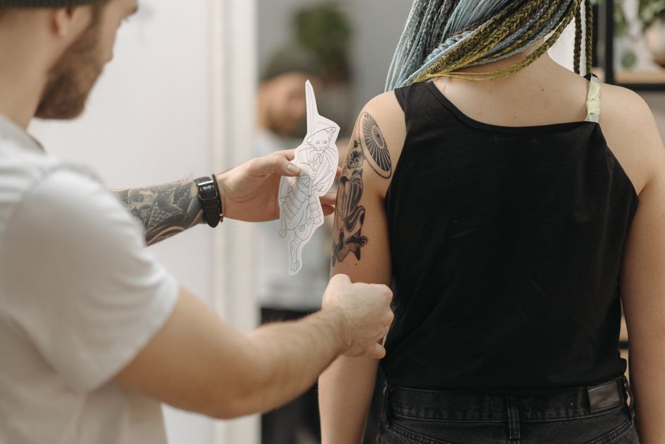 Tattoo artist preparing design on woman's arm in contemporary studio setting.