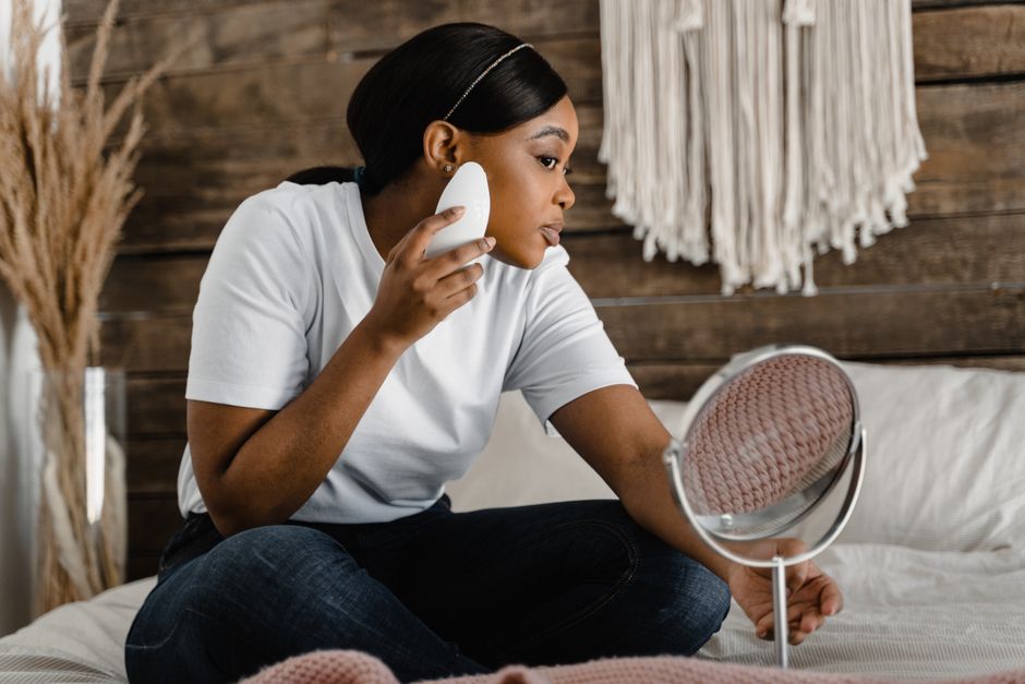 Woman in a cozy home setting using a facial roller for skincare routine.