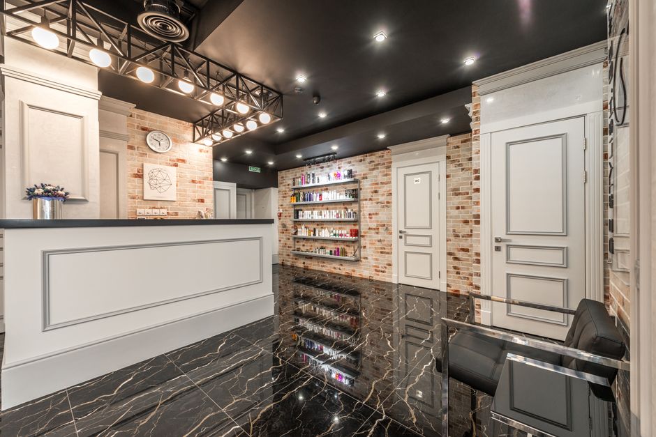 White reception counter with flowers placed in stylish beauty salon with doors and shelves with various cosmetology supplies at brick wall
