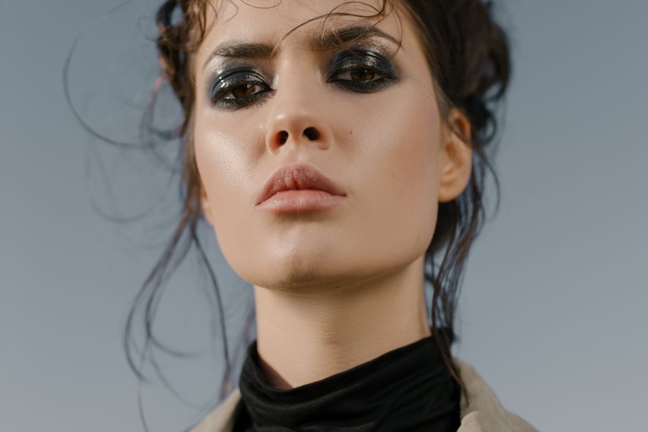 Close-up portrait of a woman with intense eye makeup and strong facial expression outdoors.