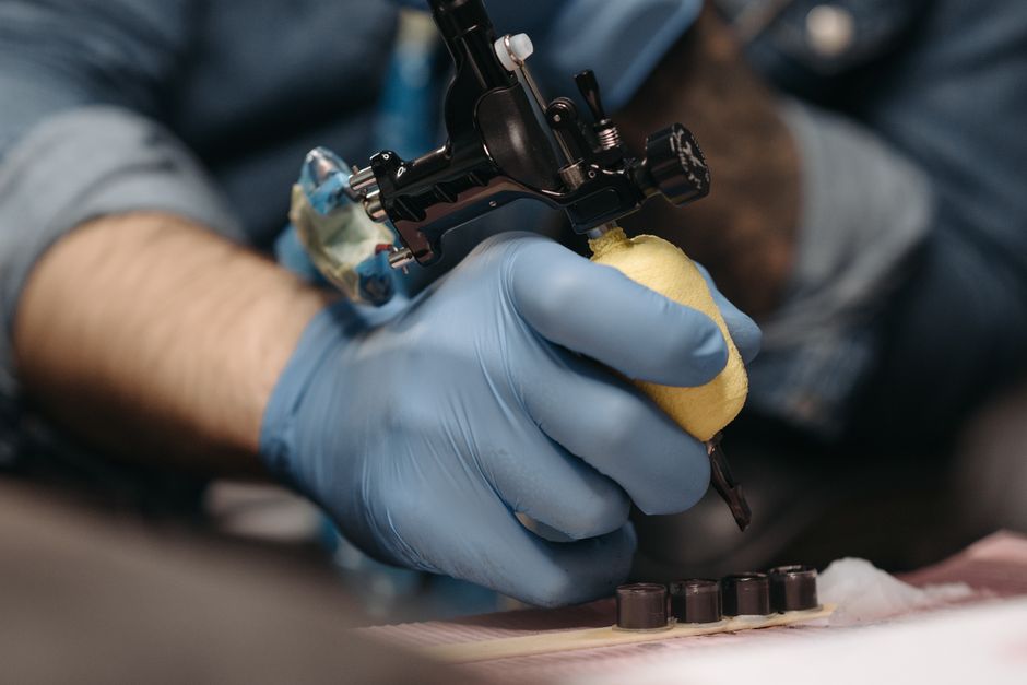 Tattoo artist with gloves operates a tattoo machine in a tattoo parlor setting