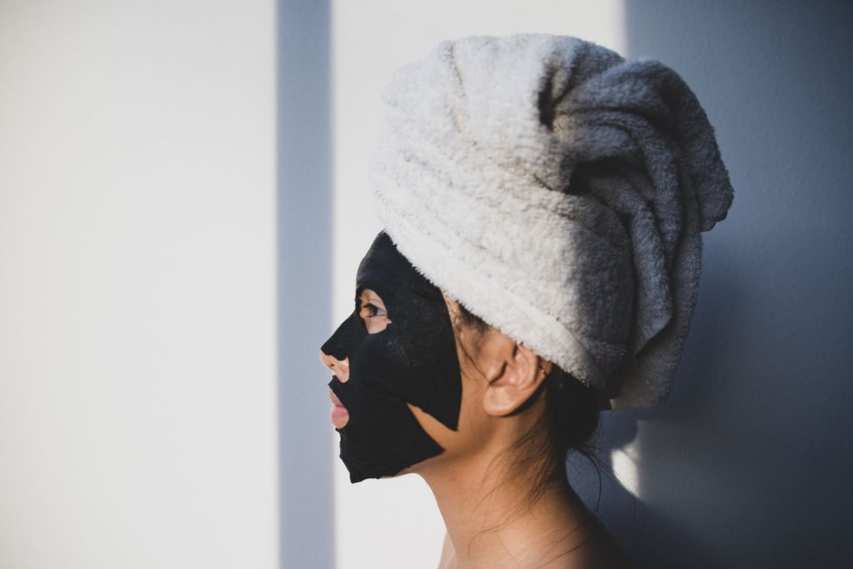 Woman wearing a black facial mask and towel turban, side profile in natural lighting.
