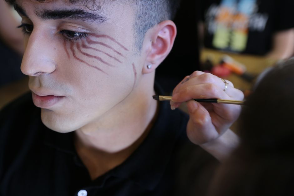 Close-up of an artist applying detailed face paint to a young man.