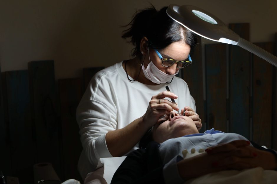 Professional cosmetologist applying eyelash extensions in a salon setting under focused lighting.