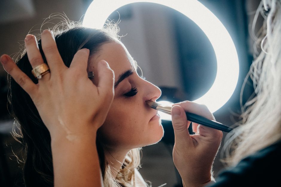 Close-up of a woman receiving makeup under a ring light by a professional artist.